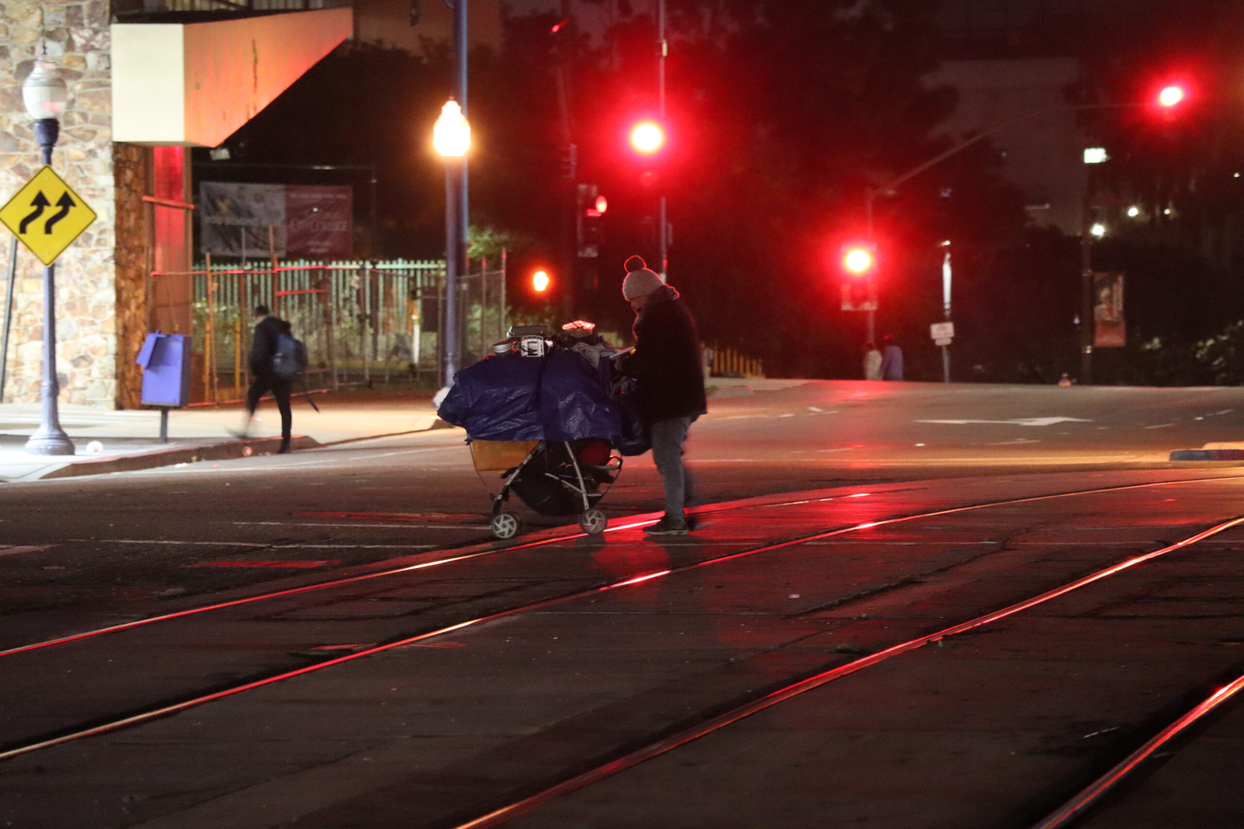 An unhoused resident stands with their cart on the metro rails in downtown San Diego.
