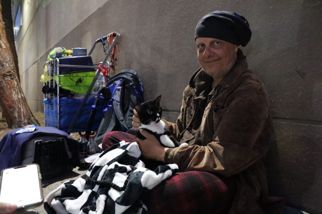 A man names Sean Thom and his cat, Sebastian, are photographed sitting on the side of a street in downtown San Diego.